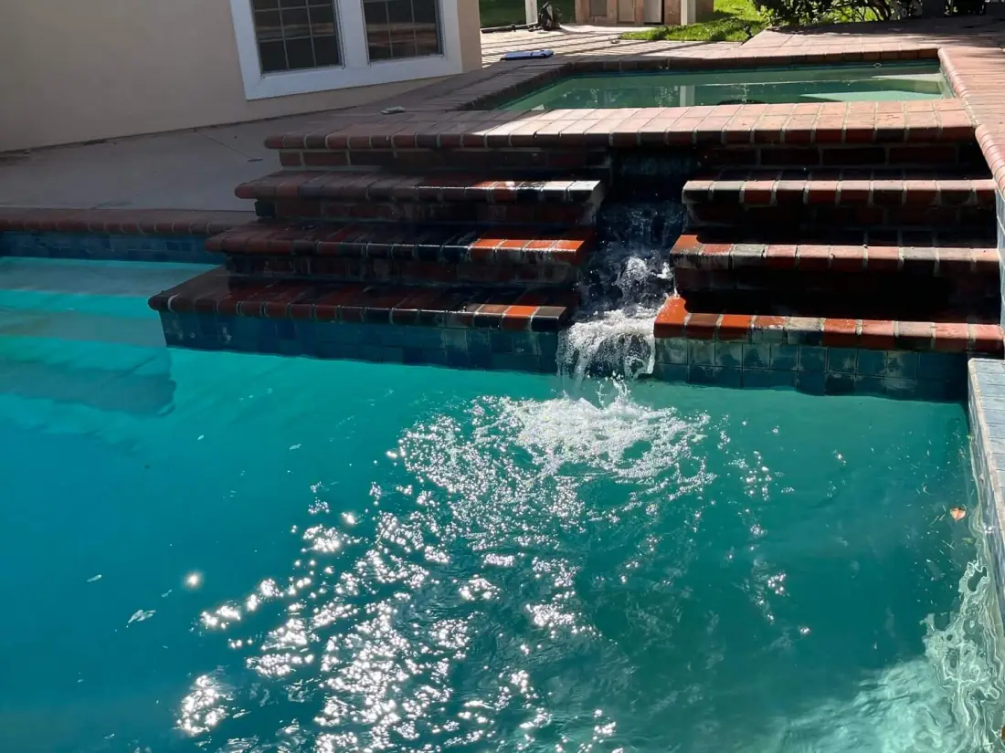 Water spilling from a raised spa down brick steps into the pool