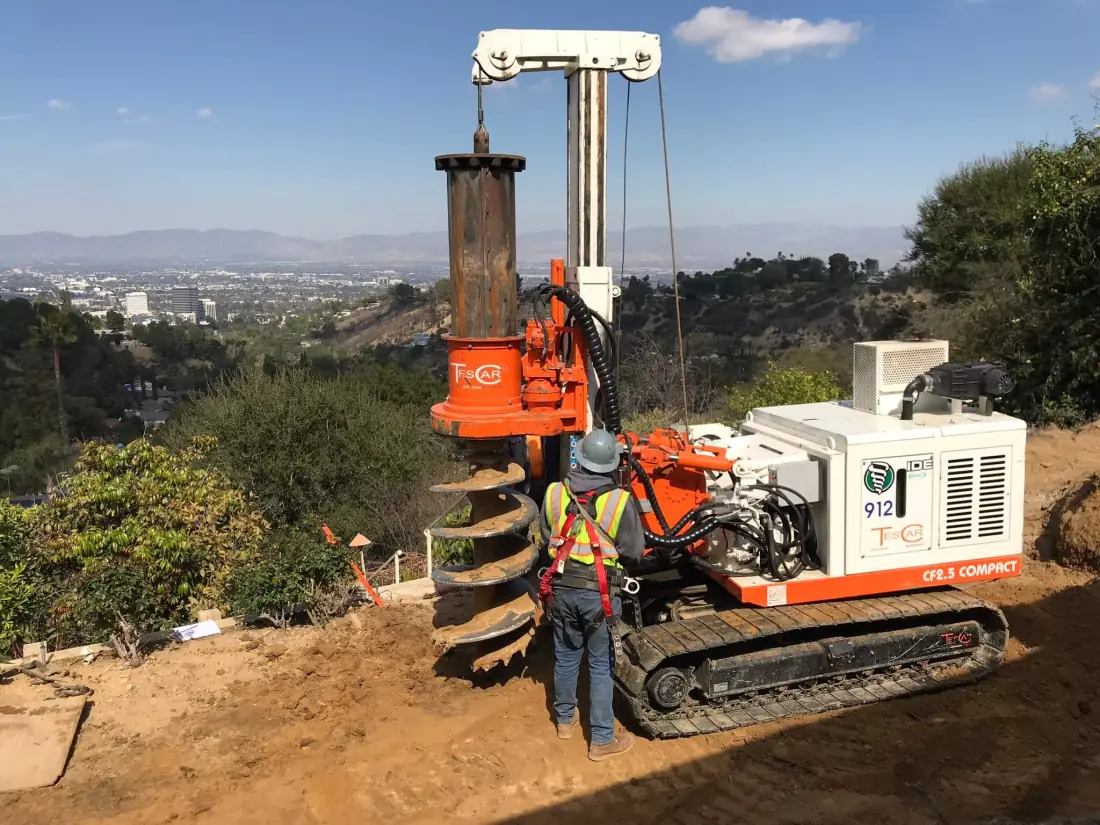 Drilling rig boring foundation piers on a hillside lot for a new pool