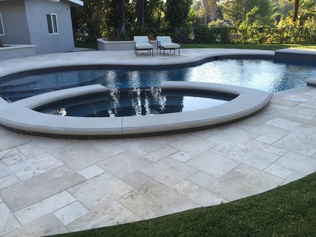Freeform pool with a raised round spa and a travertine deck