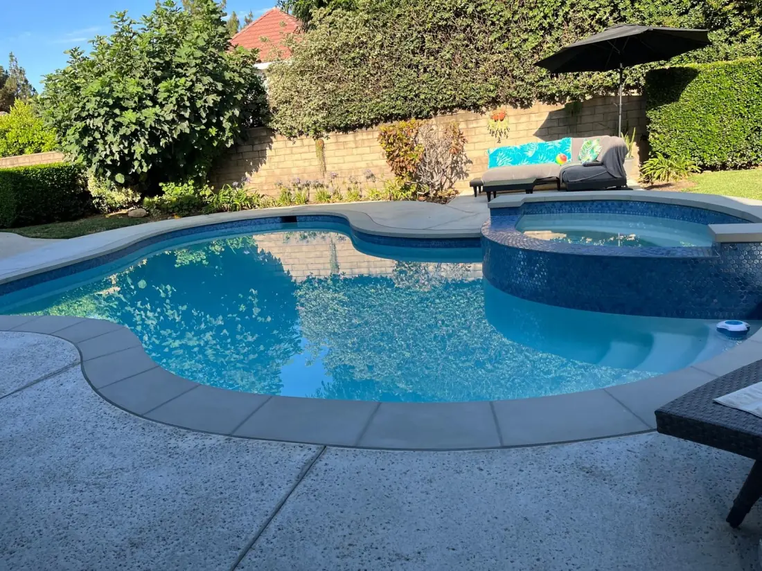 West Hills 1 Freeform pool with a raised spa finished in blue glass tile and a concrete deck