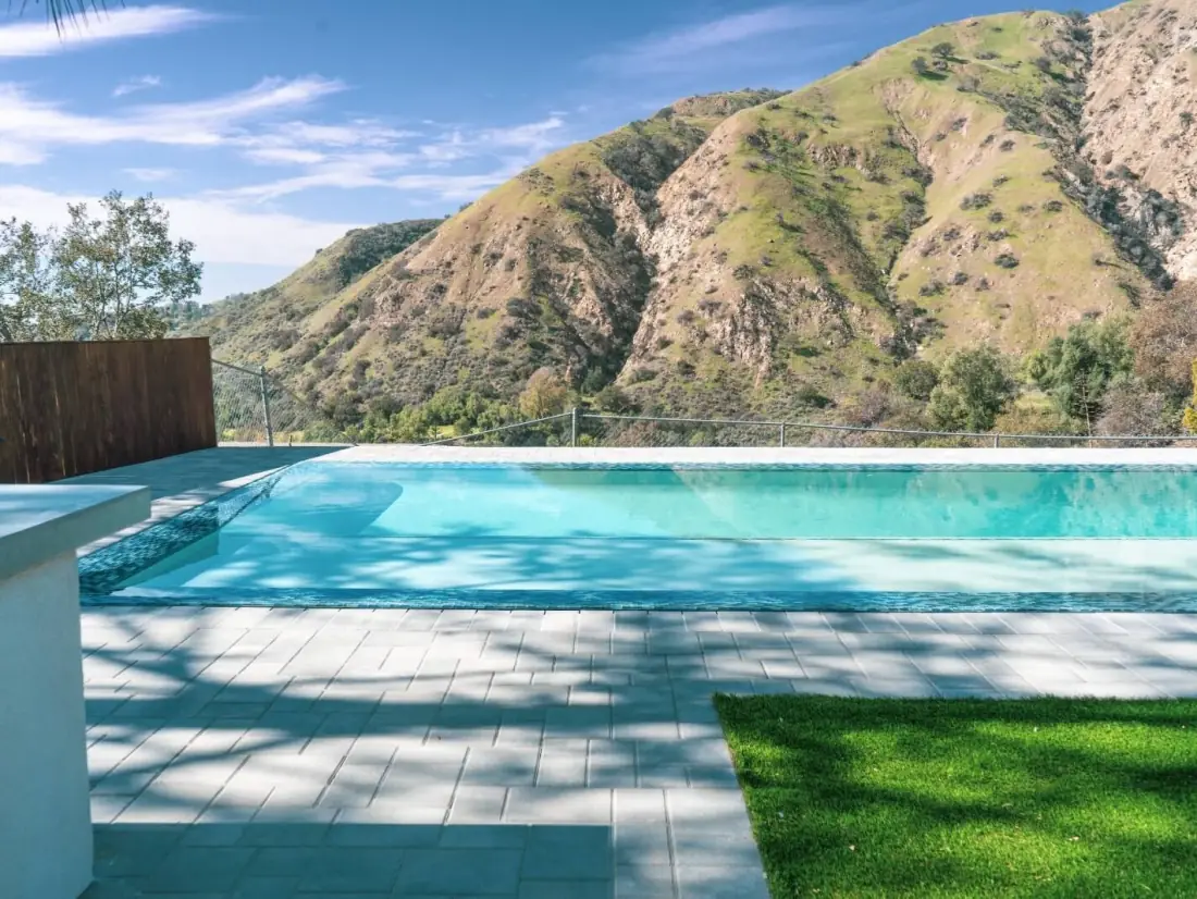 Infinity-edge pool with a glass tile wall below the mountains