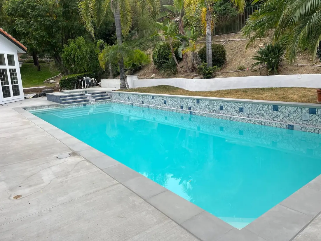 Finished rectangular pool with new gray concrete coping, a glass tile waterline and a concrete deck