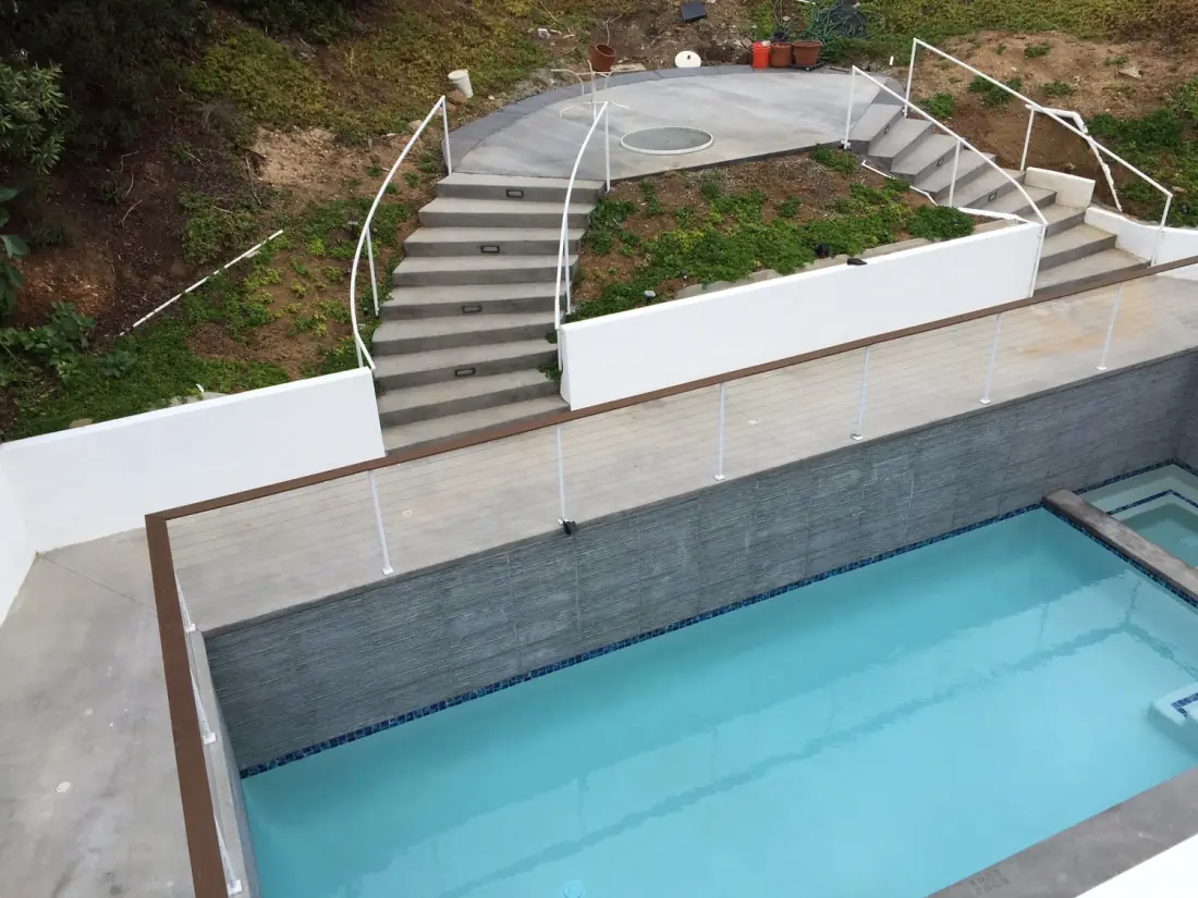 New hillside pool with a gray tile wall and glass railings, seen from above