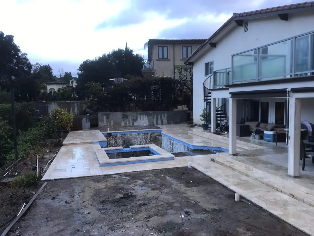 Pool and spa mid-remodel with new travertine coping and tile, the yard still under construction