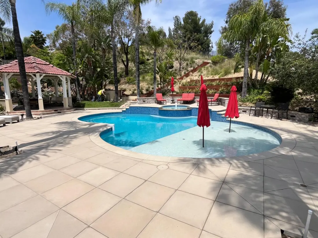 Freeform pool with a shallow Baja shelf holding two red umbrellas set in the water