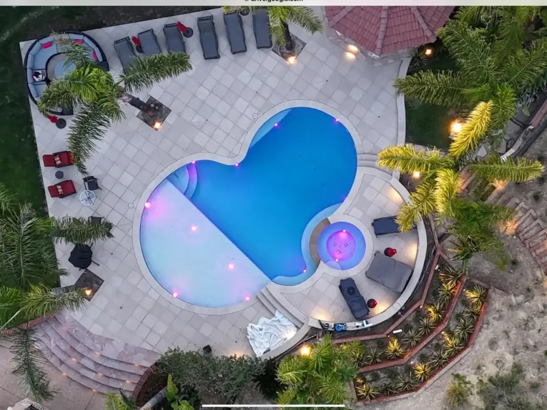 For Realtors and Home Inspectors 1 Aerial view at dusk of a freeform pool and spa with colored lights, a paver deck and a gazebo