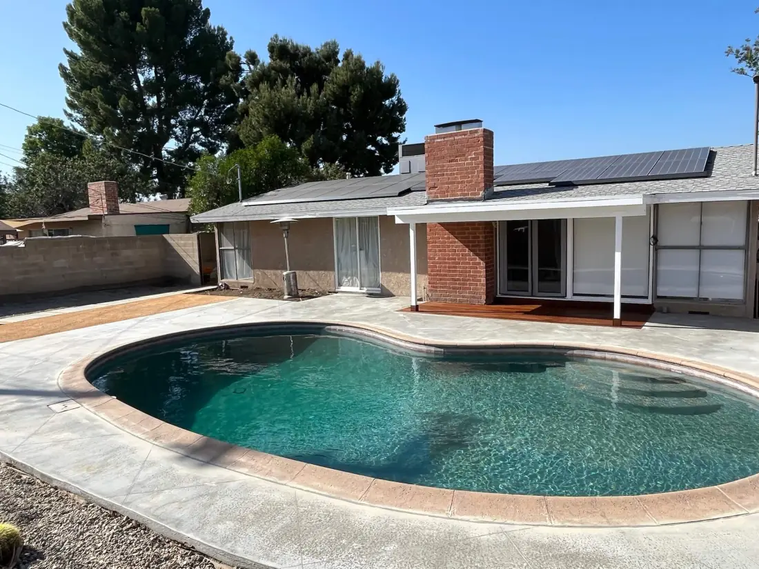 Kidney-shaped pool with a stamped concrete deck and tan coping behind a brick-chimney house