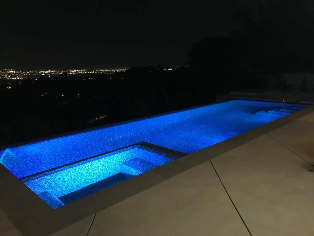 Infinity-edge pool and spa lit blue at night, overlooking city lights