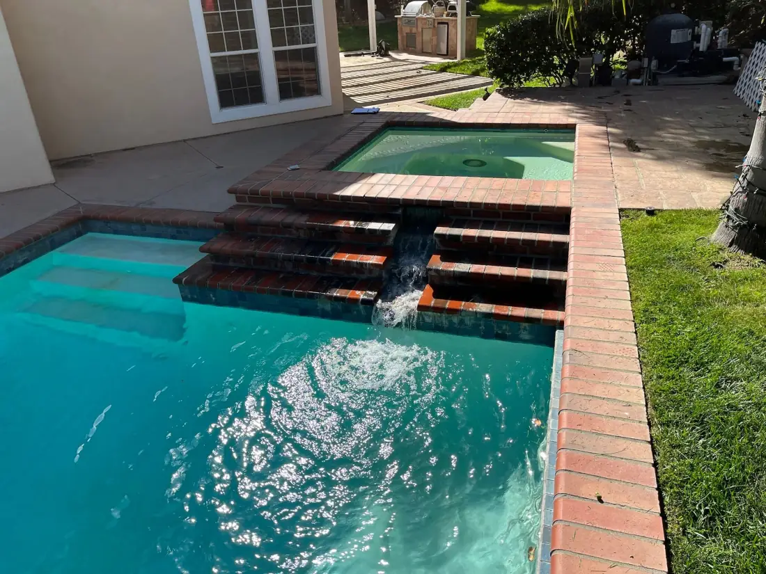Raised spa spilling over brick steps into the pool below