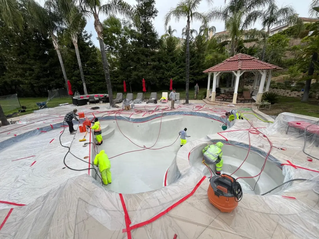 Crew preparing a pool and spa for resurfacing with the deck masked off