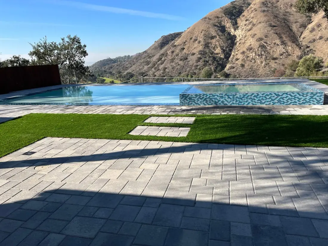 Vanishing-edge pool with a glass tile spa, paver deck and turf below the hills