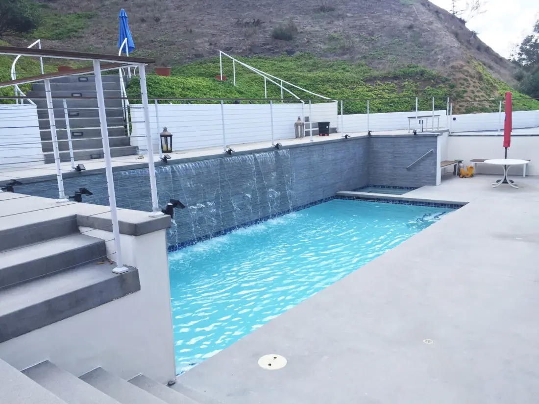 Modern pool with a row of sheer descent waterfalls spilling from a raised tiled wall