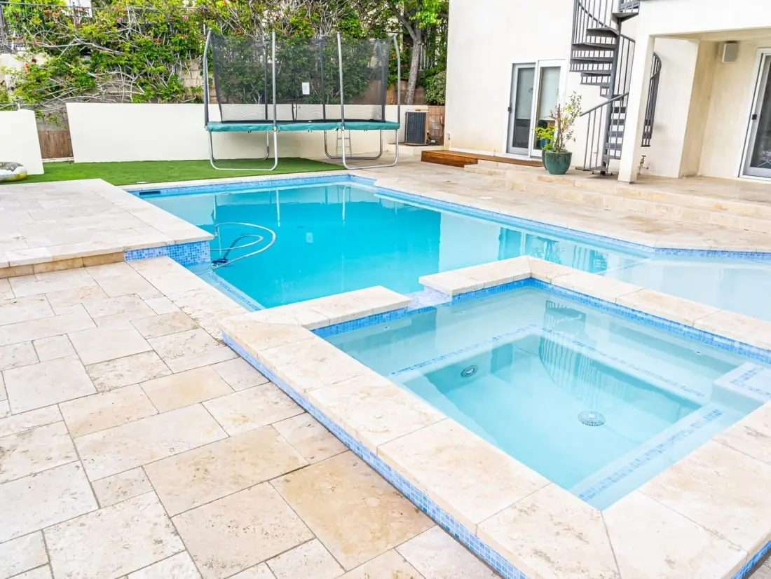 Pool with a raised spa, travertine deck and blue glass tile trim