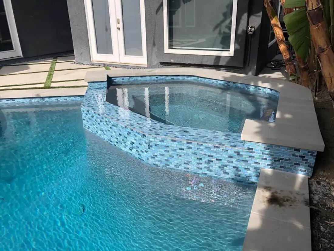 Raised spa finished in blue glass mosaic tile spilling into the pool