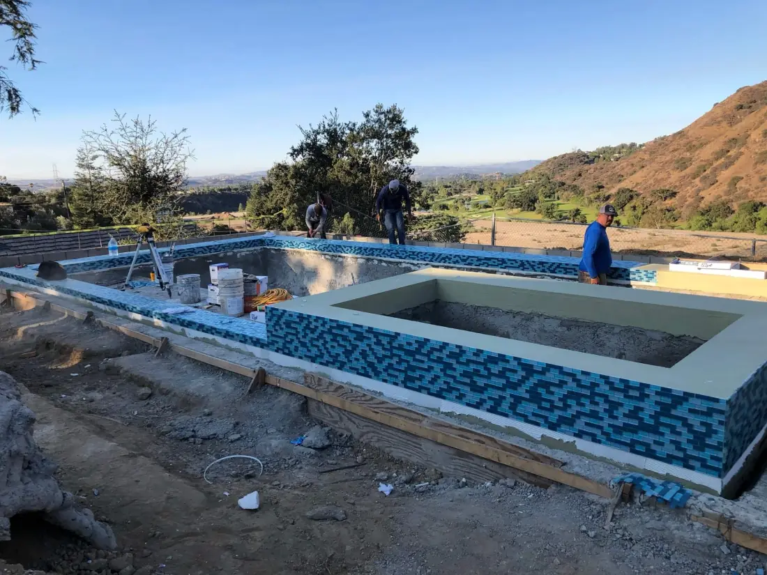 Blue and teal glass tile going onto a raised spa and pool wall during construction